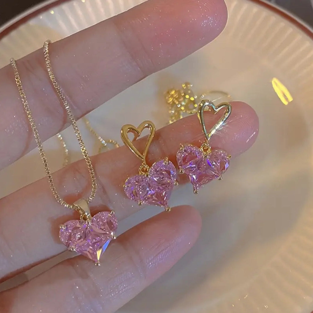 Gold necklace with pink heart-shaped pendants held by a hand on a light background